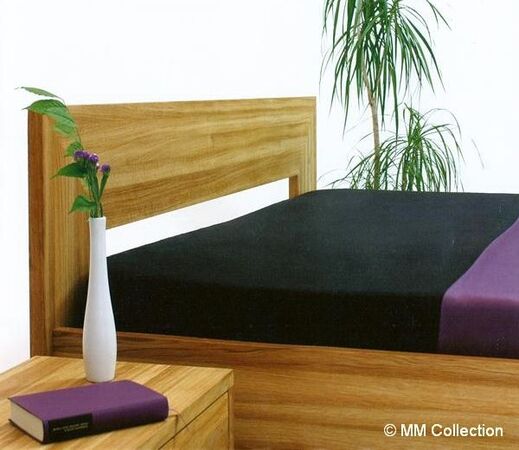 Modernes Holzbett mit schwarzer Bettwäsche, Nachttisch, Pflanze und lila Akzent.