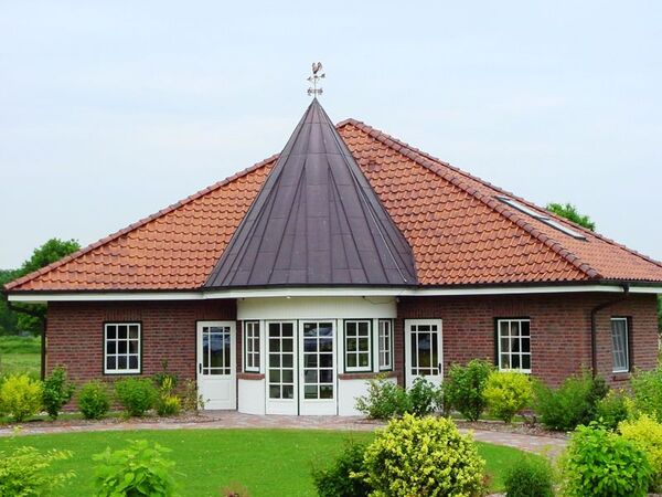 Modernes Einfamilienhaus mit rotem Ziegeldach, großer Fensterfront und gepflegtem Garten.