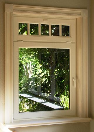 Weißer Kunststoffrahmen eines modernen Fensters mit Blick auf grüne Gartenpflanzen.