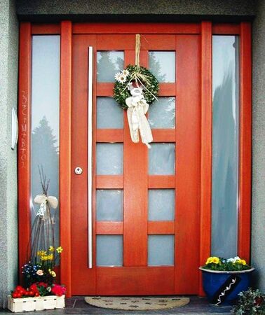 Moderne Holzeingangstür mit seitlichen Glasfeldern, Frühlingskranz und Blumendekoration.