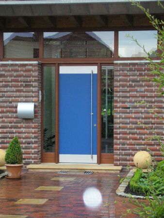 Moderne Haustür mit blauem Türblatt in einem Backsteinhaus und gepflegtem Vorgarten.